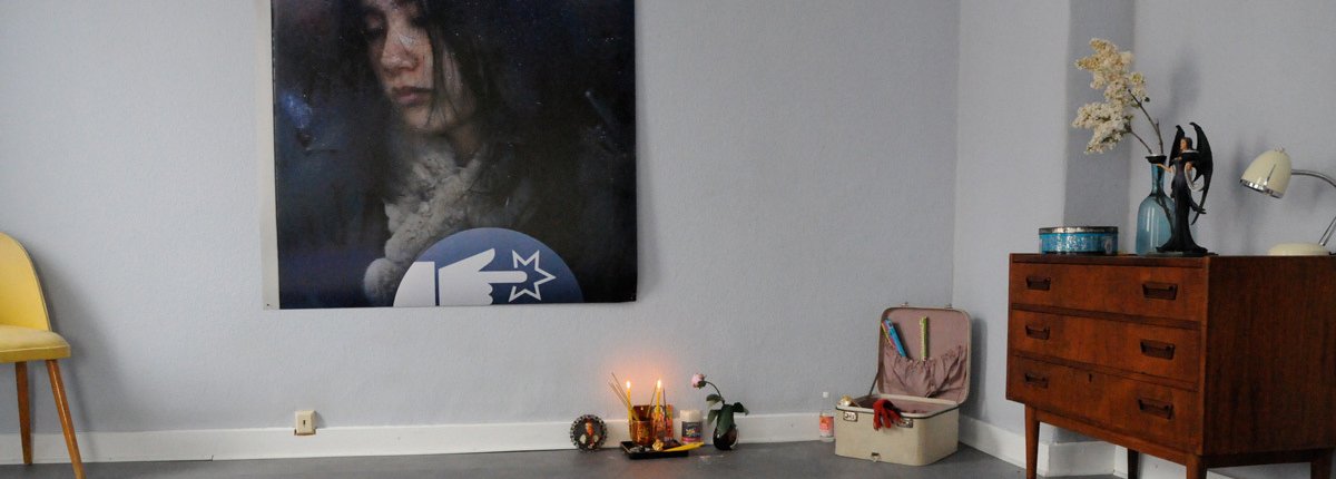 Ein minimalistischer Wohnraum mit Vintage Möbeln, großem Plakat und kleinem Altar mit Kerzen