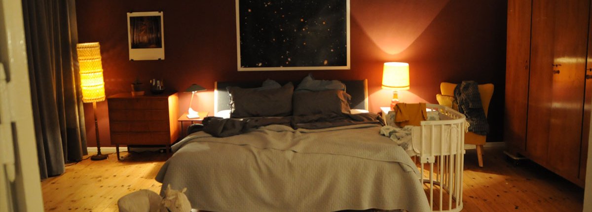 Ein Elternschlafzimmer in rot, braun, beige und rost Tönen mit stimmungsvollem Glühlampenlicht.